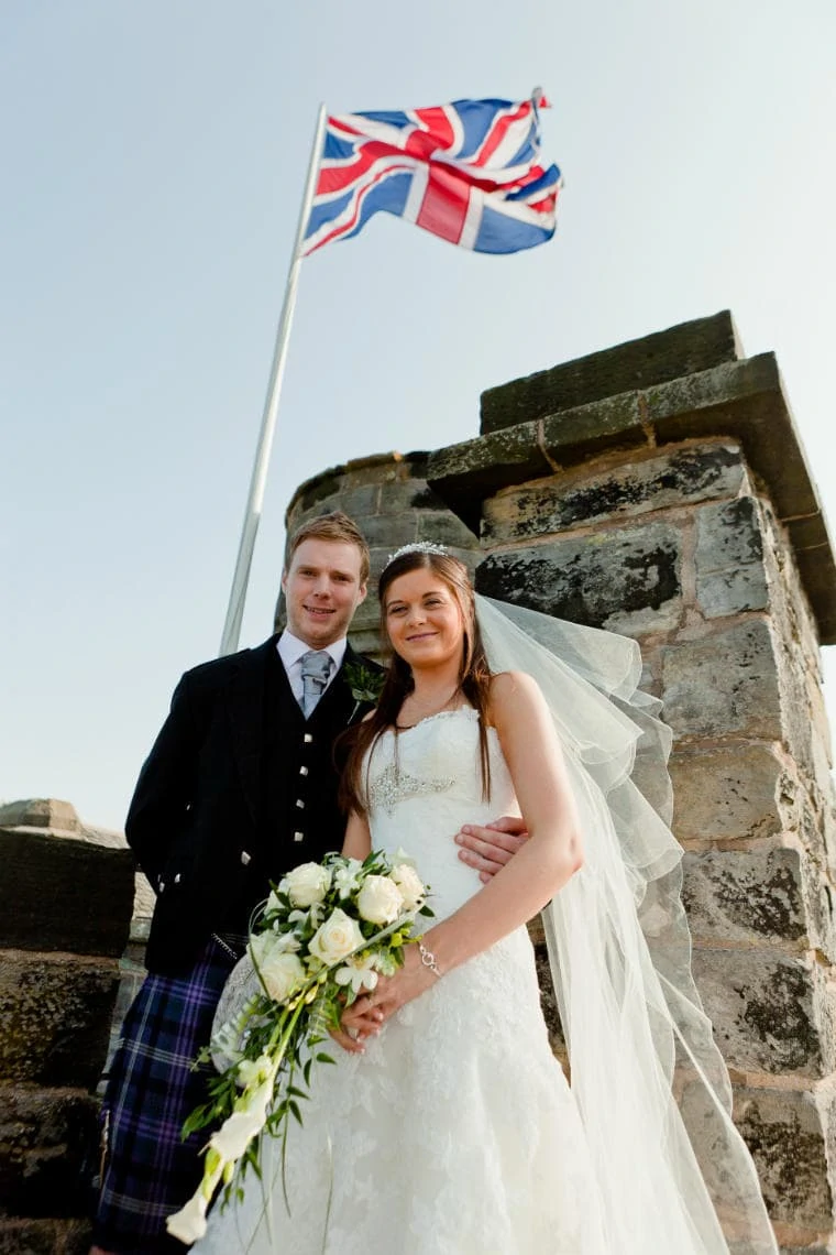 newlyweds standing beneath the Union Jack on the roof of the Auld Keep