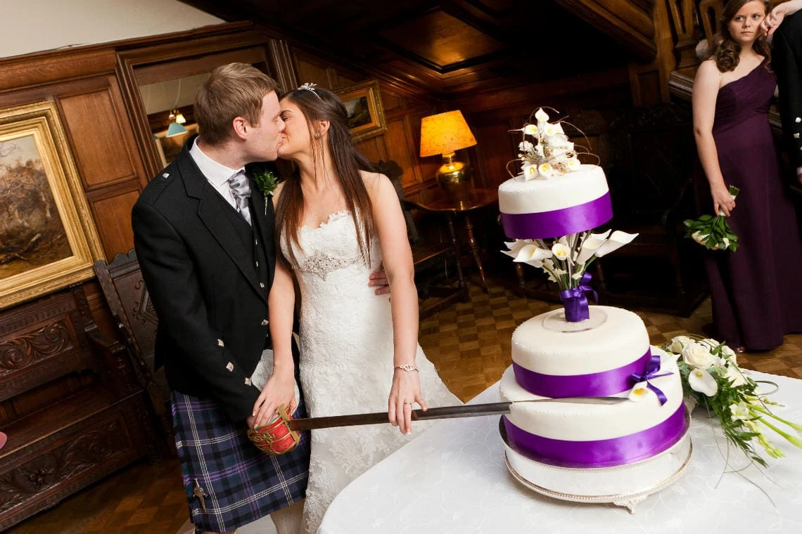 newlyweds kiss as they cut the cake with a ceremonial sword in the Main Hall