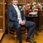 groom wearing a blue suit and brown shoes sitting in the Billiards Room
