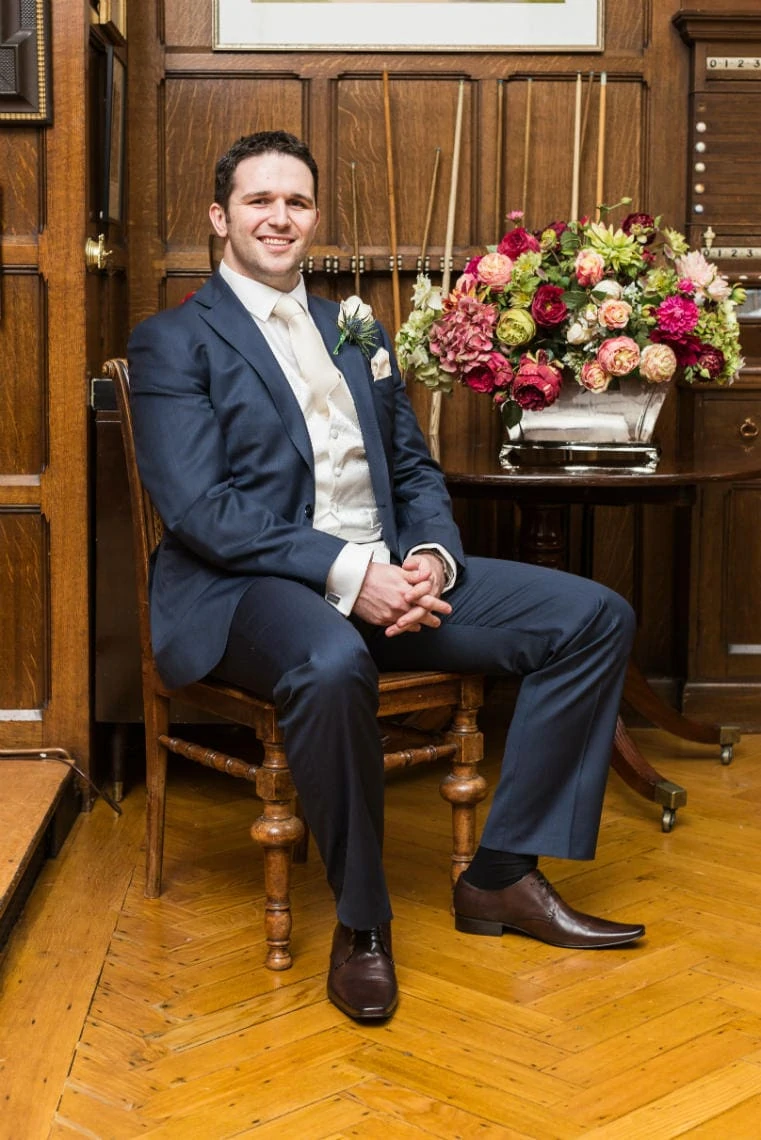 groom wearing a blue suit and brown shoes sitting in the Billiards Room