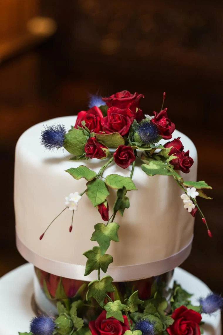 white wedding cake decorated with red roses and thistles