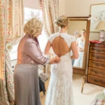 mother of the bride helps her daughter into her dress in the Winter bedroom