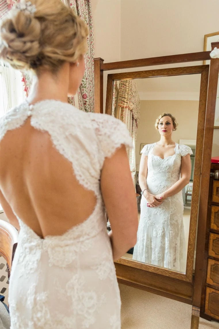 beautiful bride wearing a white dress looking into a full-length mirror in the Winter bedroom