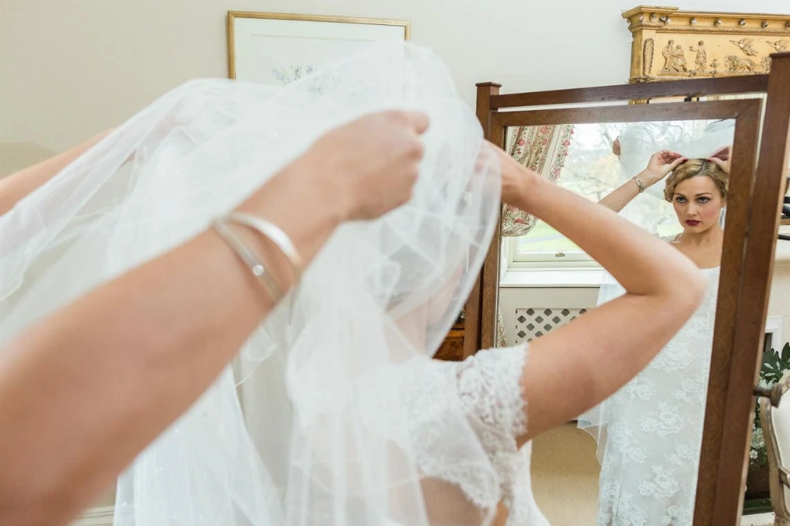 bride puts on her veil in front of a mirror in the Winter bedroom