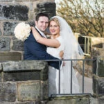 newlyweds looking at the camera and smiling on the roof of the Auld Keep