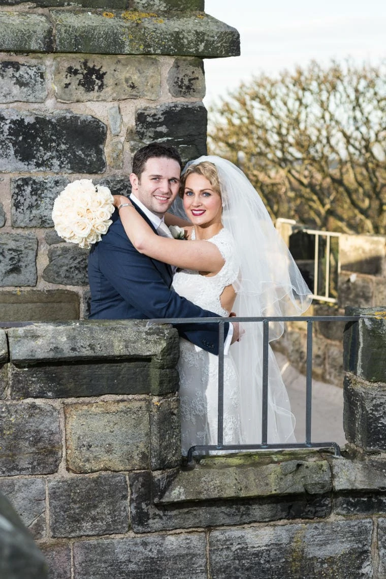 newlyweds looking at the camera and smiling on the roof of the Auld Keep