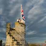 newlyweds embrace next to the Union Jack on the roof of the Auld Keep at Dundas Castle