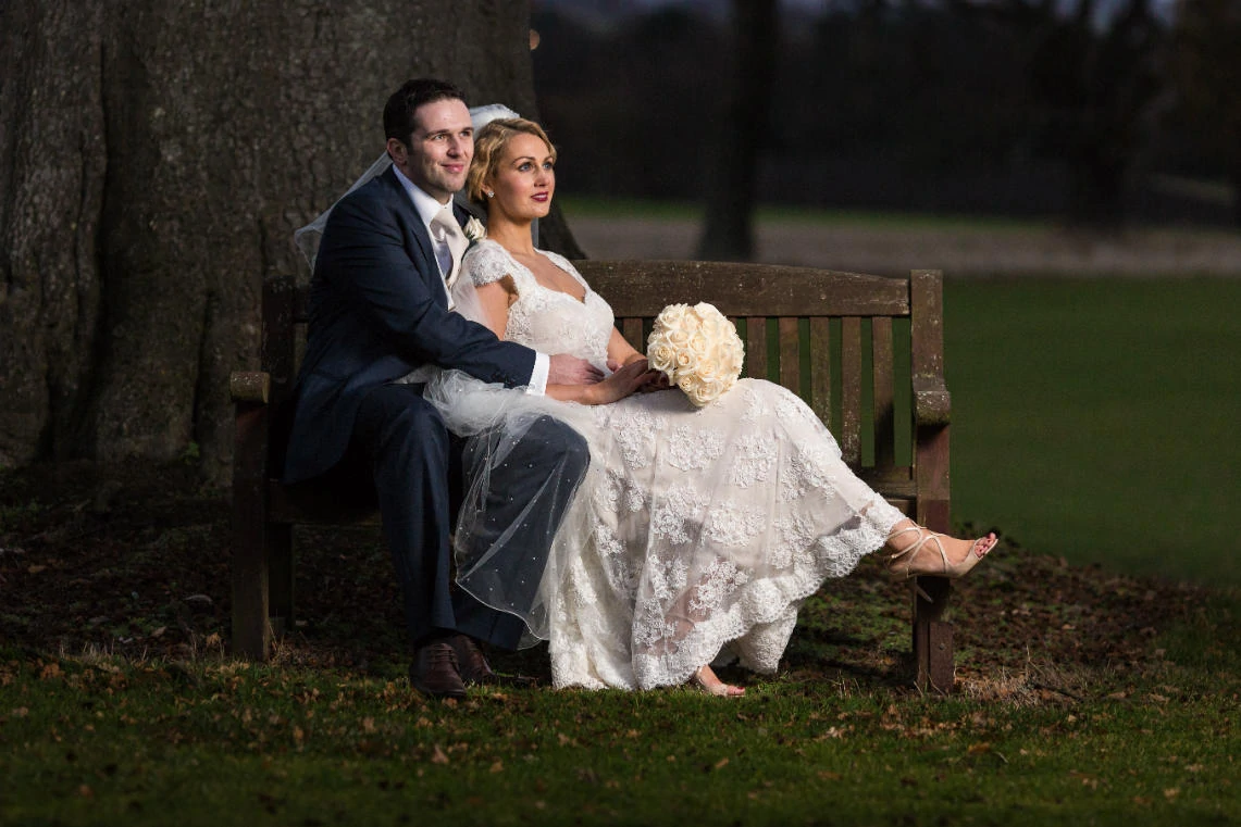 newlyweds embrace on the wooden bench on the lawn