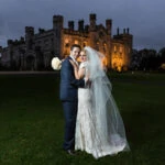 newlyweds embrace at dusk in front of the castle on the lawn with the castle lit up in the background