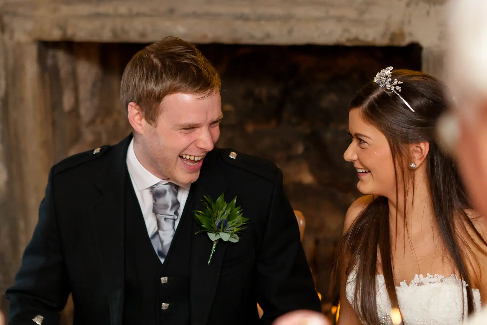 A smiling groom in a military uniform and a bride with a tiara sitting together, sharing a joyous moment.