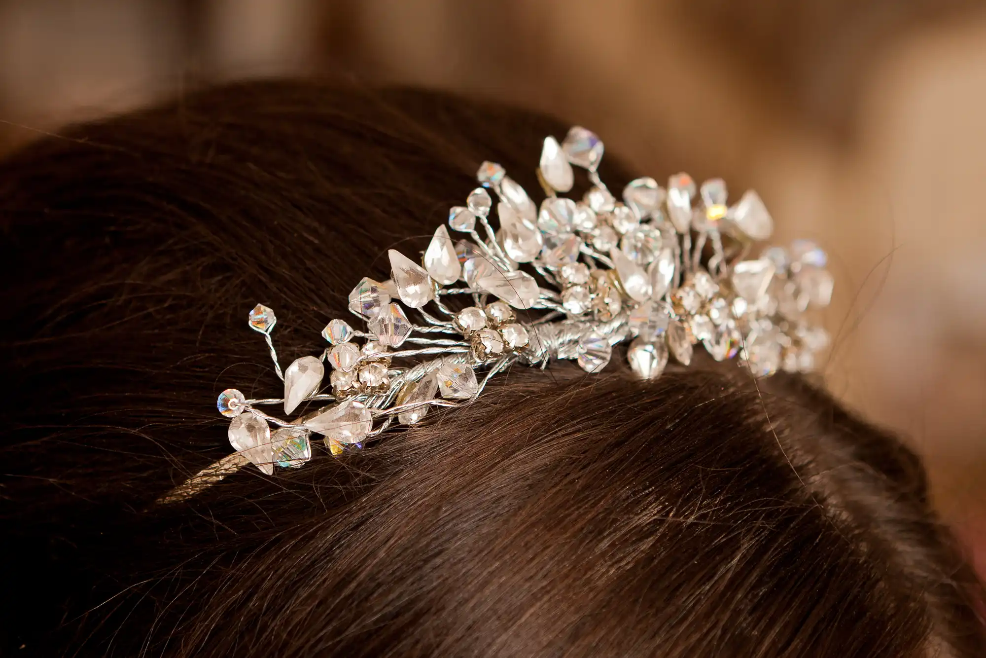 Close-up image of a sparkling crystal tiara on a person's brunette hair, highlighting intricate details and reflections.