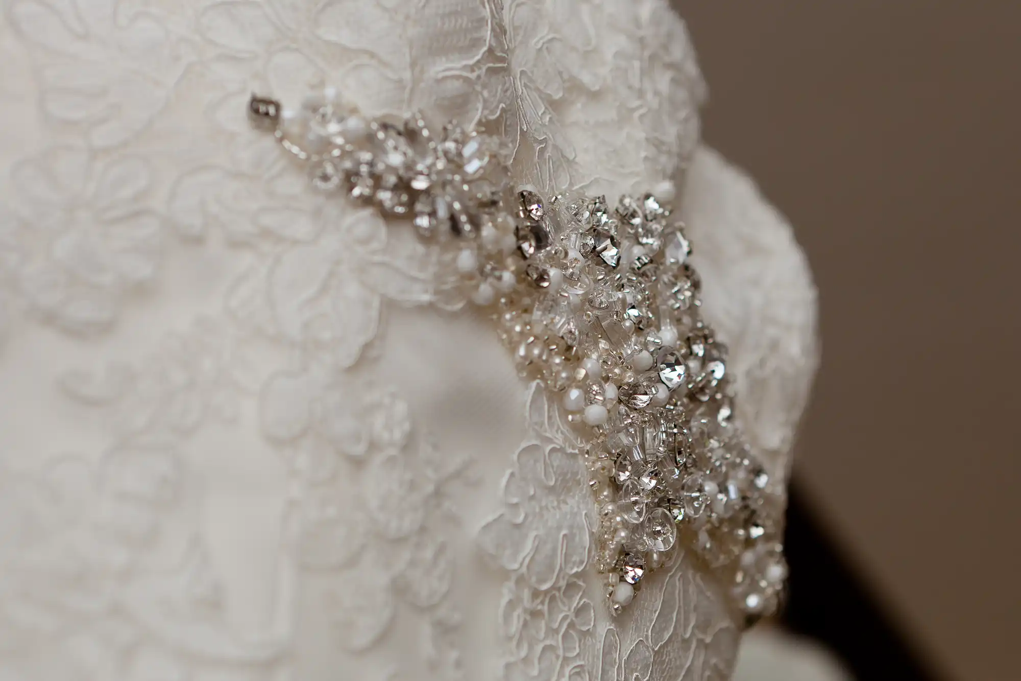 Close-up of a detailed wedding dress with lace fabric and intricate beading on the sleeve.