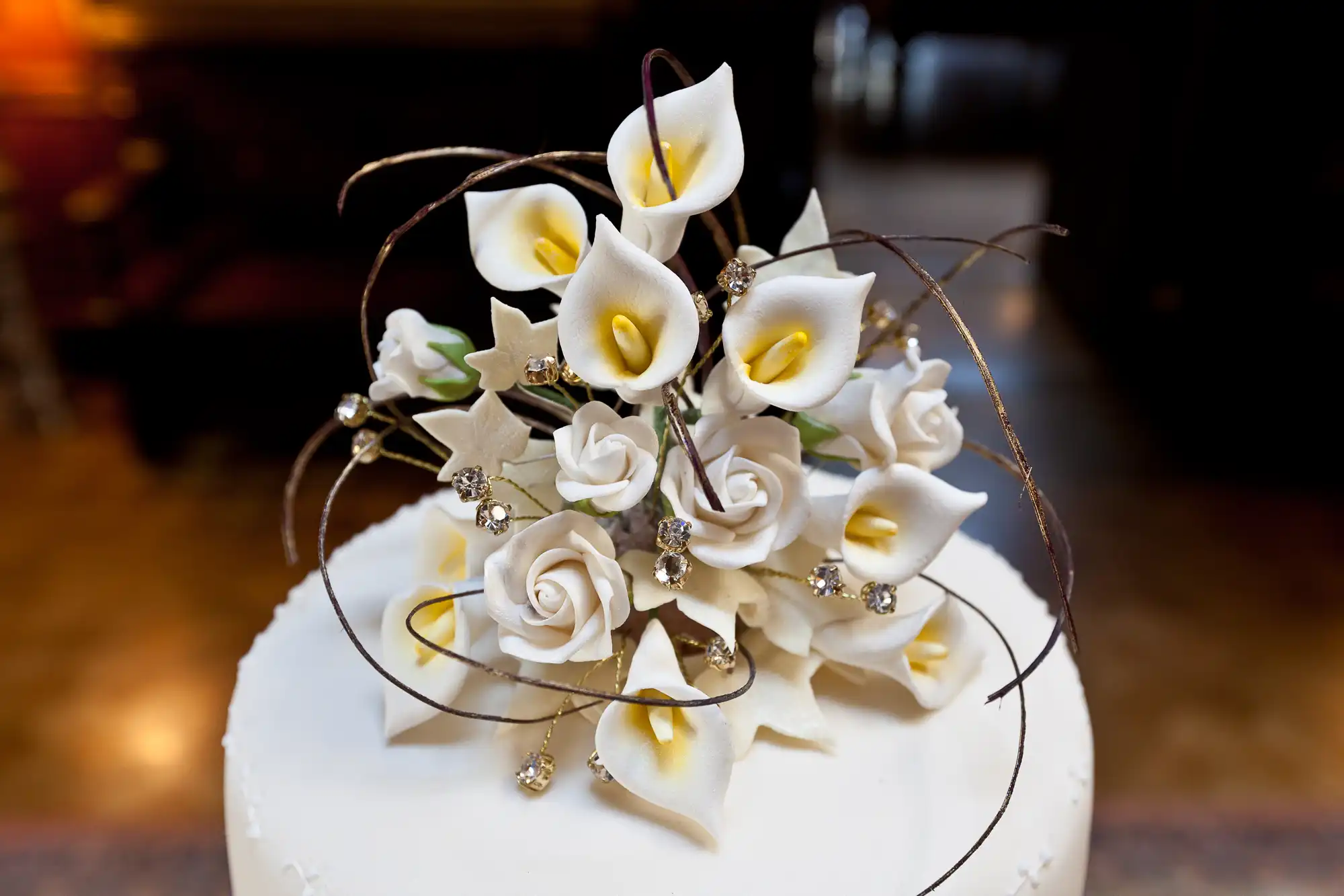 Elegant wedding cake topped with white calla lilies and roses, accented with delicate crystals and swirling dark branches.