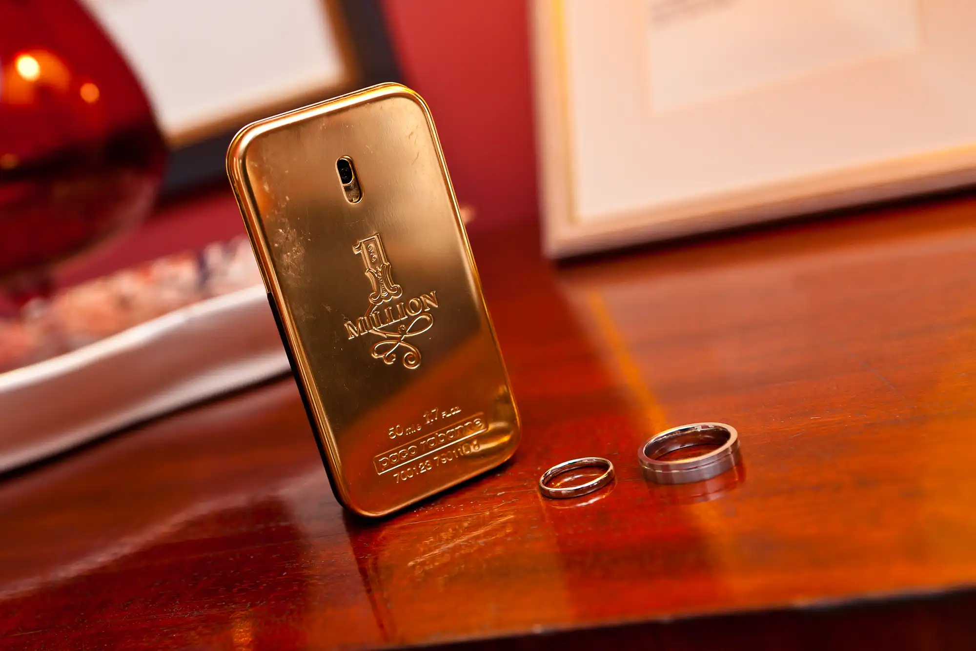 A golden cologne bottle and two wedding rings placed on a wooden surface.