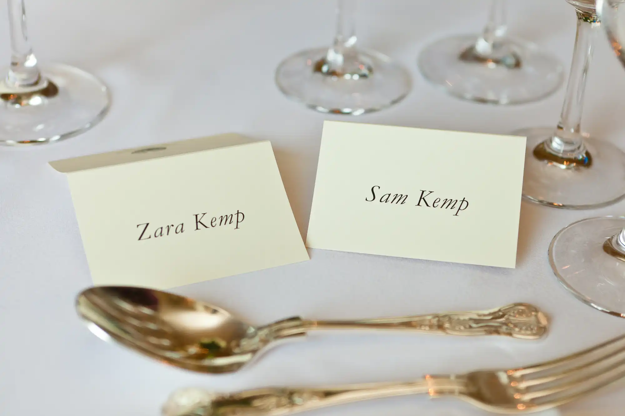 Place cards with names "zara kemp" and "sam kemp" on a formal dining table with silverware and wine glasses.