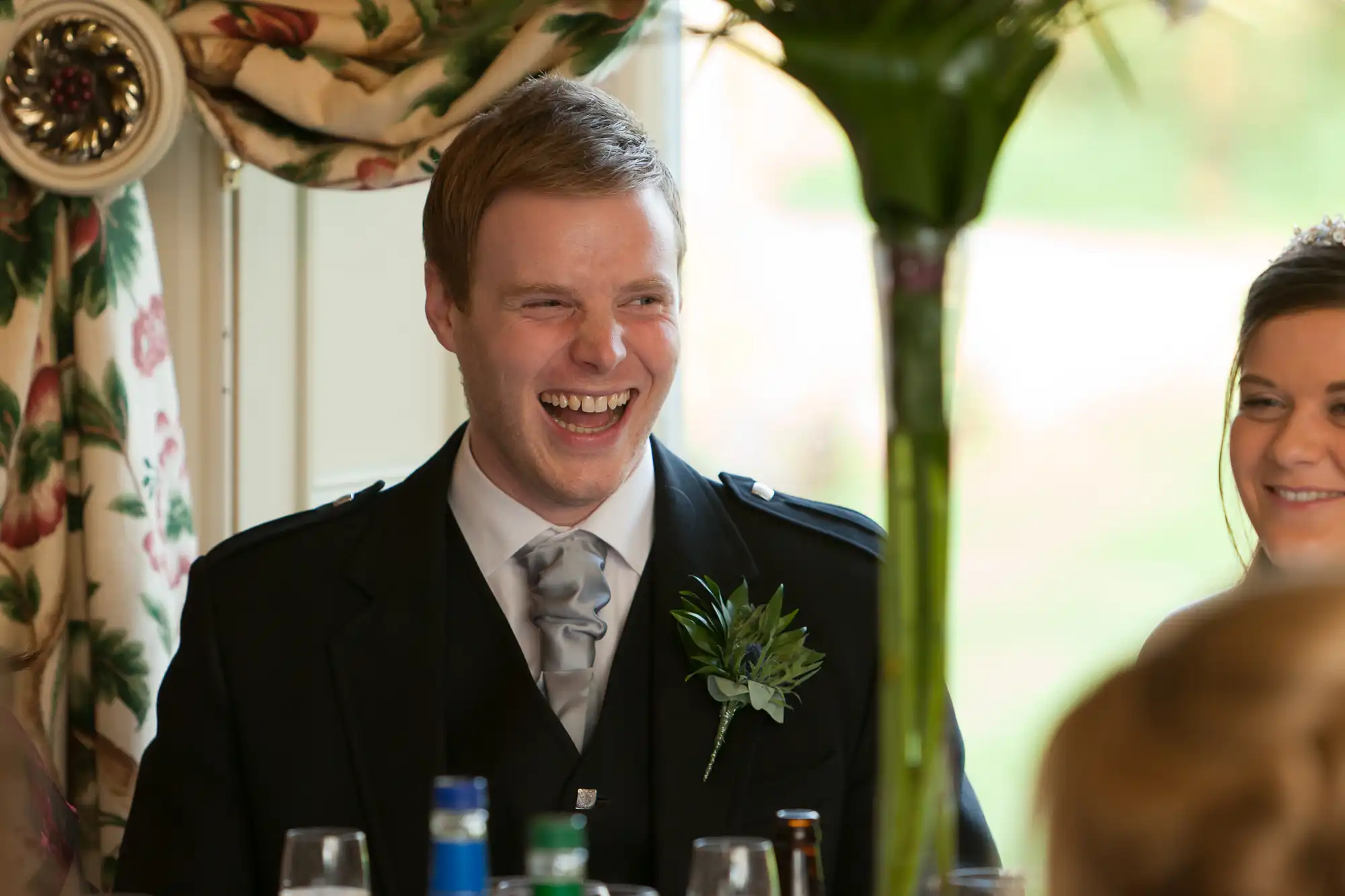 Man in a suit laughing joyously at a formal event, with a woman smiling beside him.