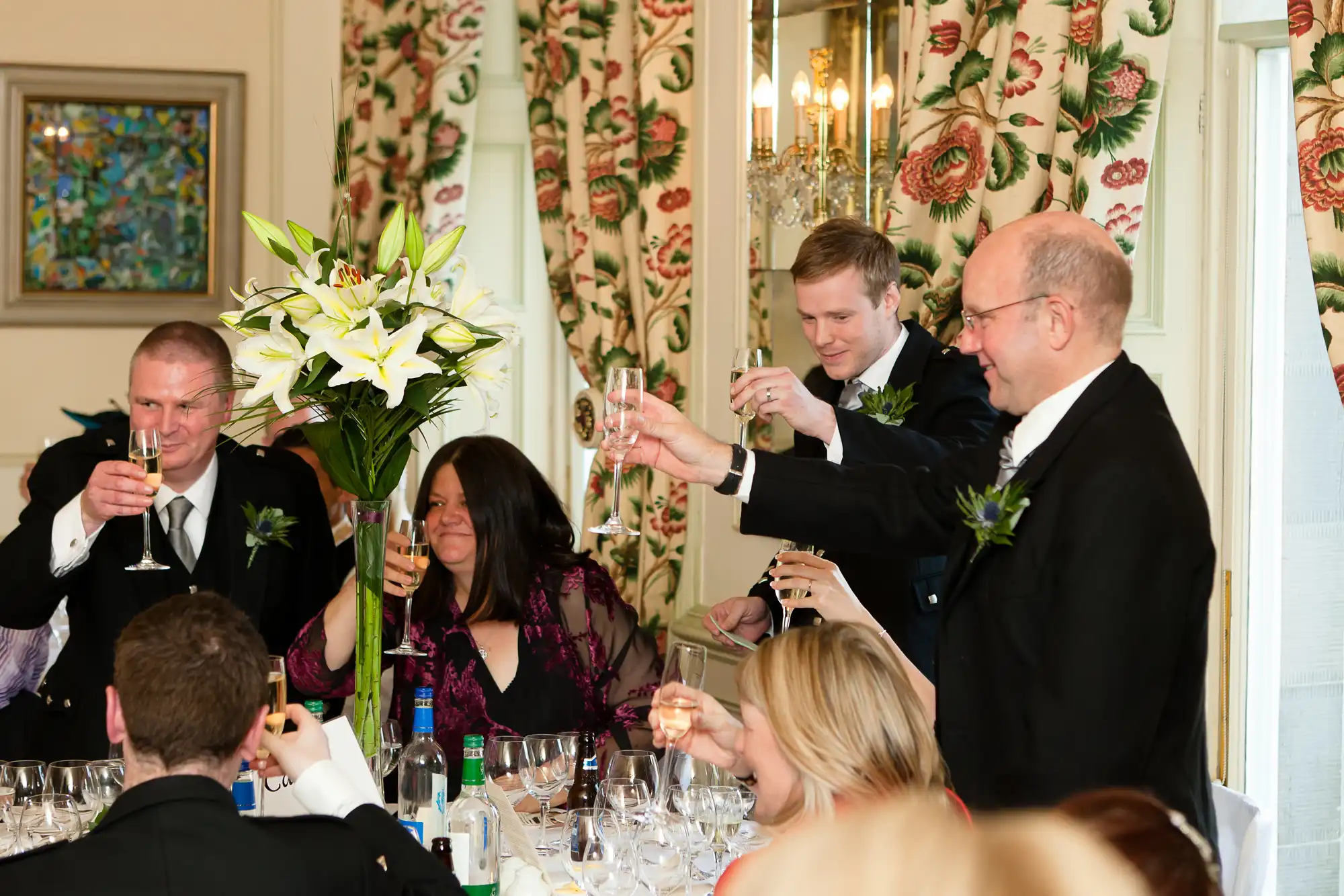 Group of people raising a toast at a formal dining event, with floral decorations and elegant table settings.