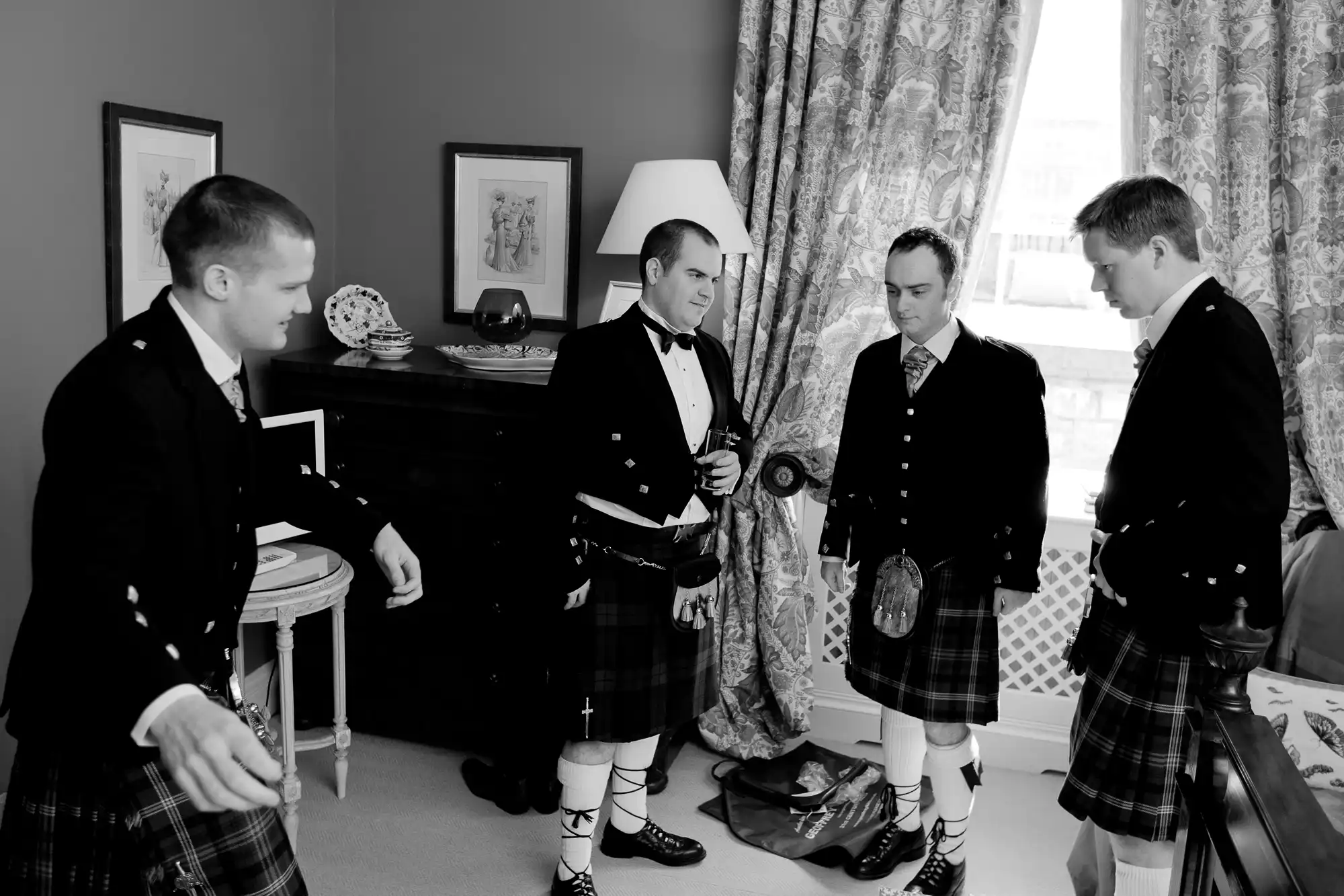 Four men in traditional kilts having a conversation in an elegantly decorated room.