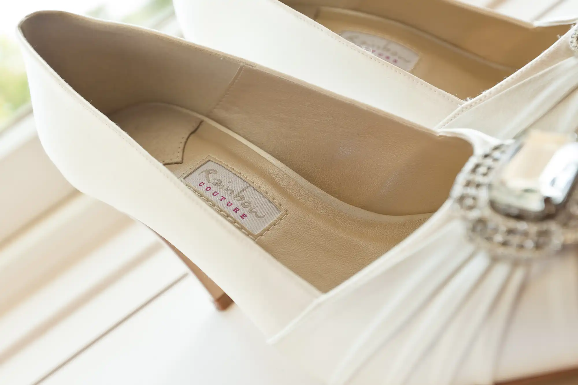 Close-up of elegant white high-heeled shoes with a label reading "rainbow couture" inside.
