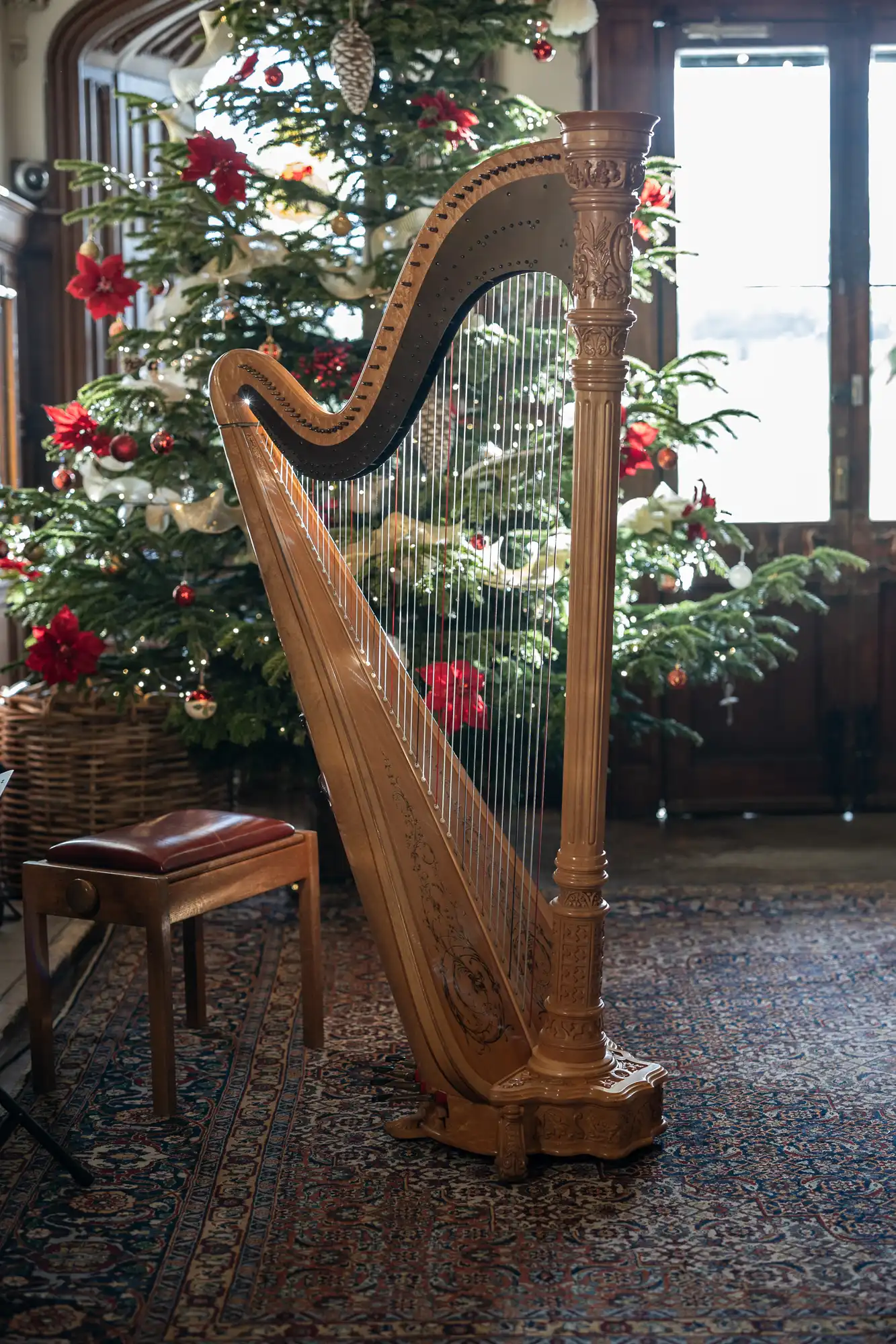 A wooden harp stands beside a stool in front of a decorated Christmas tree, with red and white ornaments, in a room with a patterned rug.