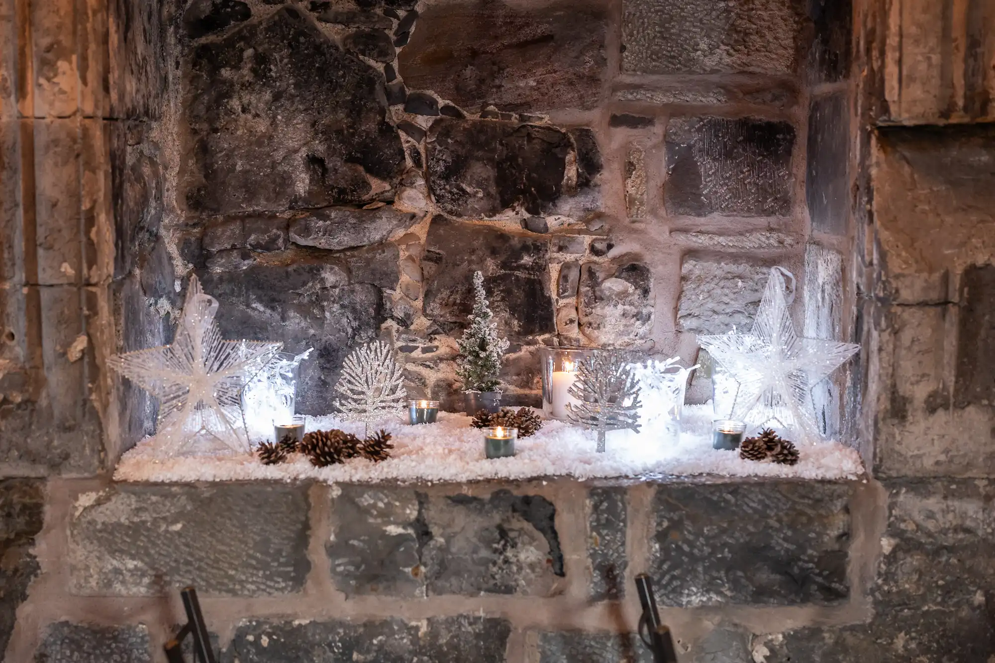 A stone alcove decorated with small lit trees, star ornaments, candles, and pinecones, all arranged on a bed of artificial snow.