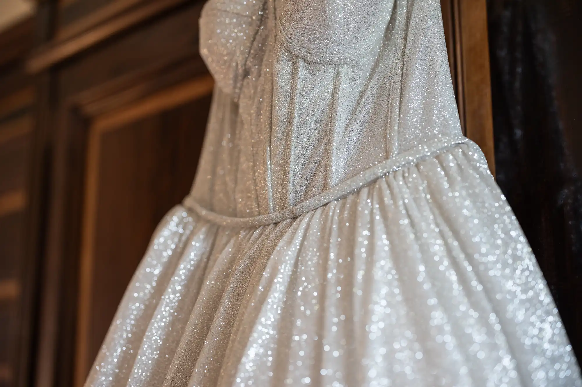 A close-up of a silver glittery dress hanging on a wooden wardrobe door.