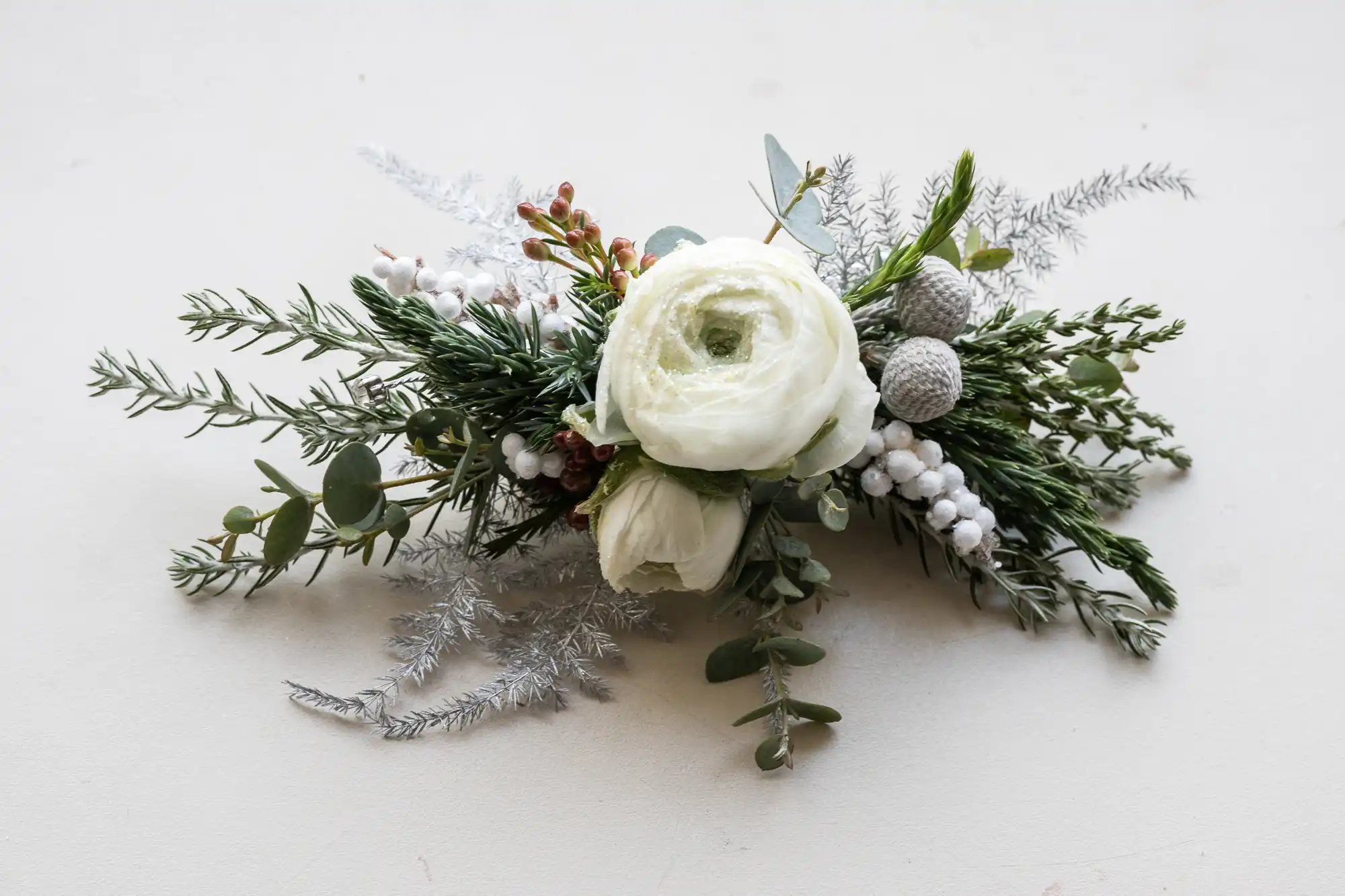 White roses and green foliage with white berries arranged on a light background.