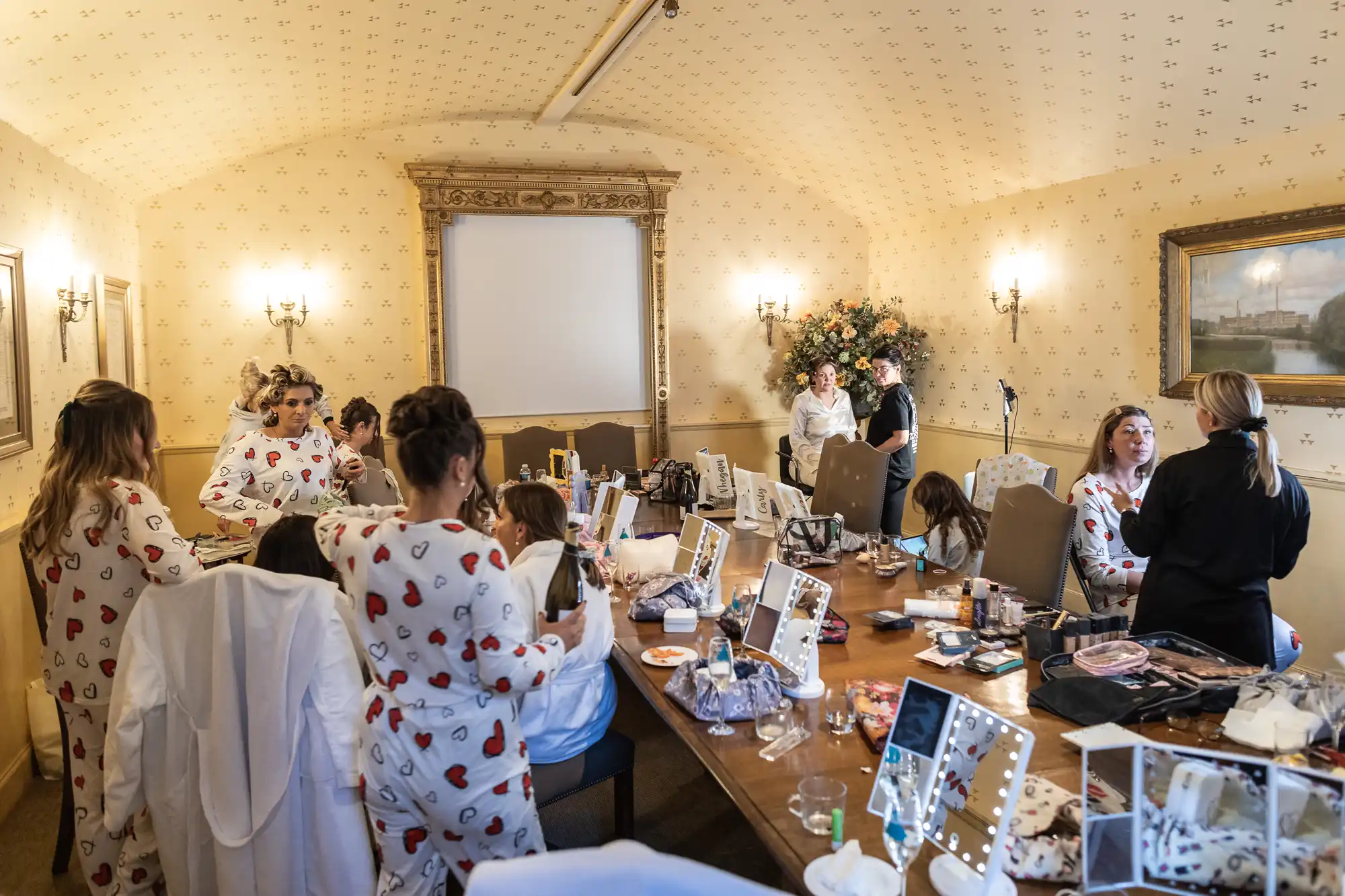 A group of people in matching pajamas are getting ready in a room with makeup and hair styling tools spread out on a long table.