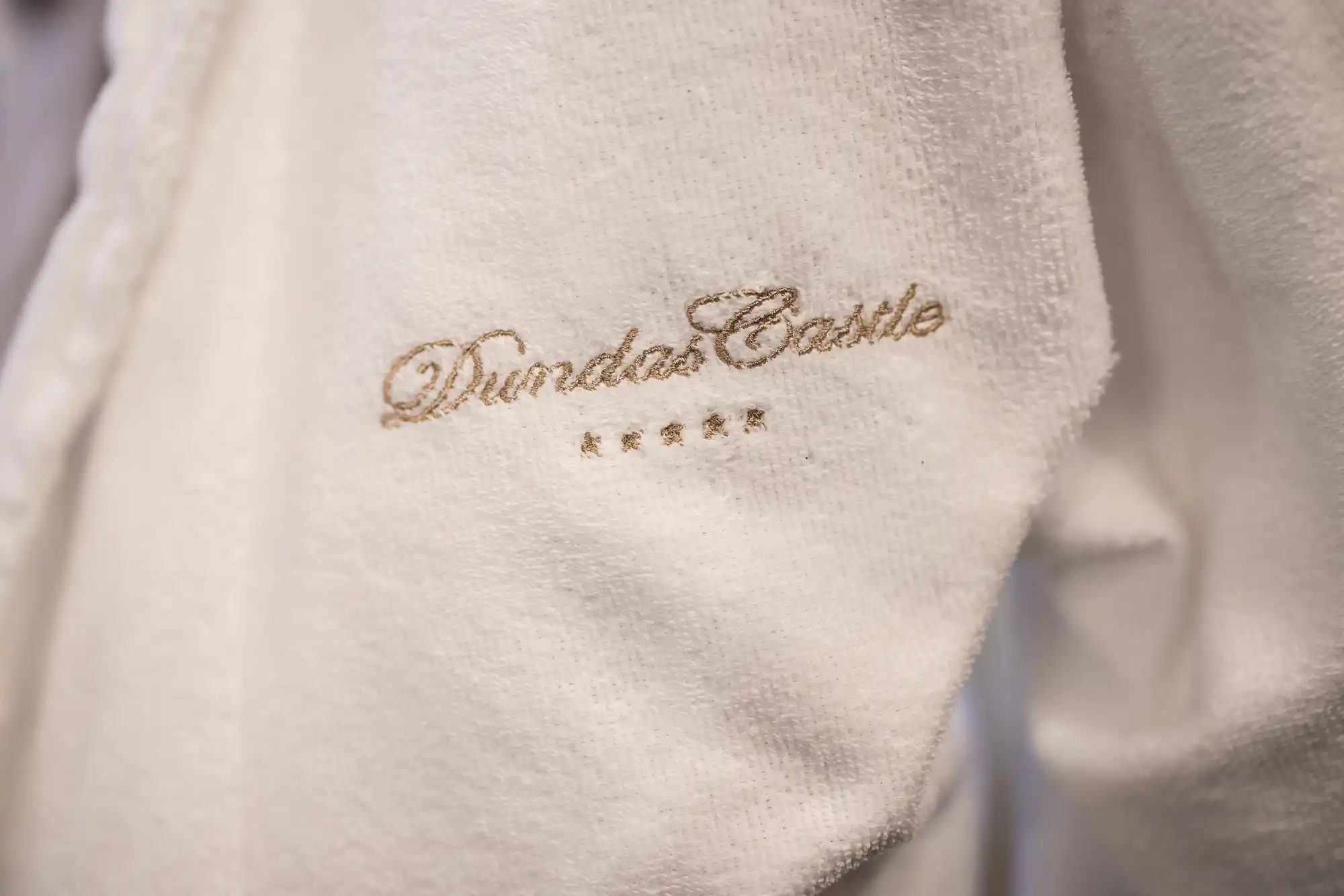 Close-up of white fabric with "Dundas Castle" and four stars embroidered in gold thread.