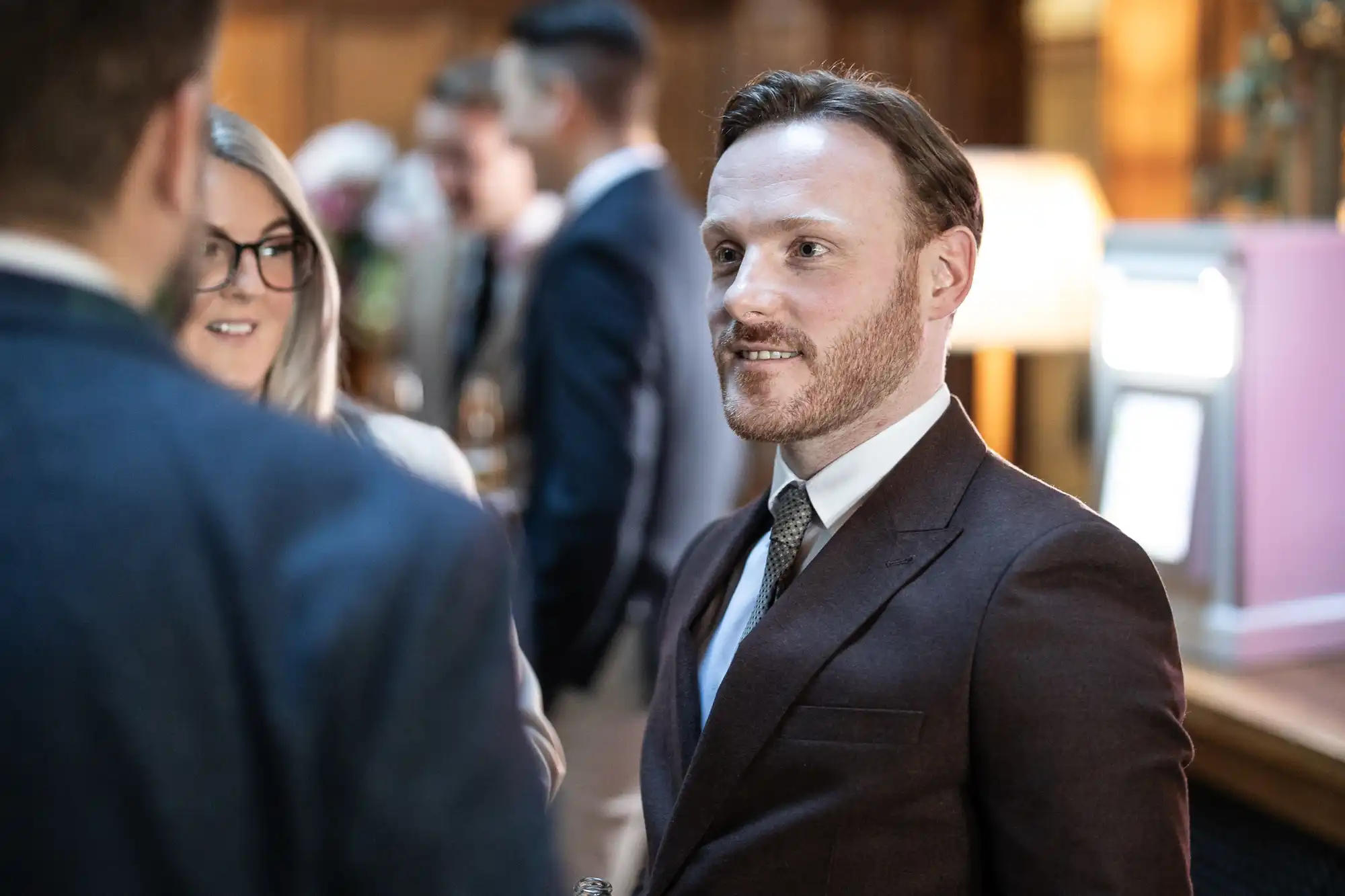 A man in a suit and tie converses with a group of people at a formal indoor event.