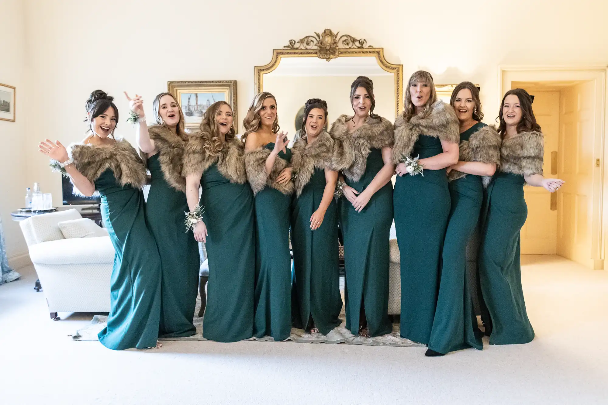 A group of nine women wearing green dresses and fur stoles stand in a room, posing for the camera.