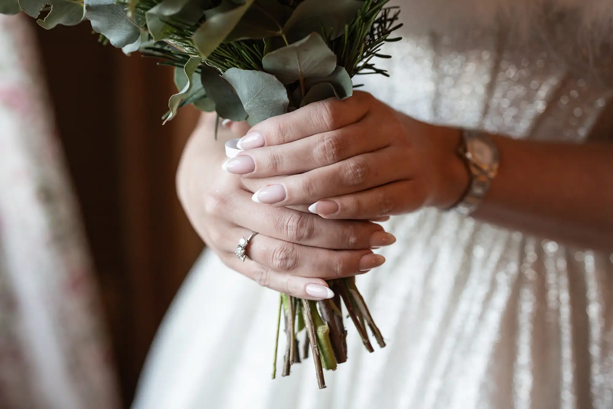 A person holds a bouquet of greenery and eucalyptus with both hands, wearing a watch and a ring.