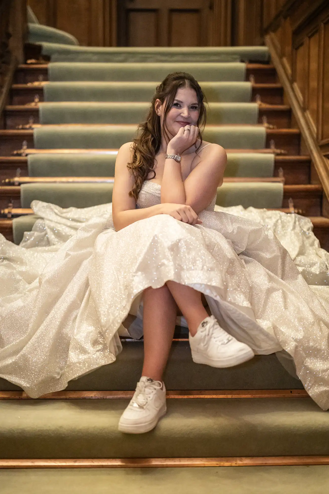 A young woman in a sparkly gown and white sneakers sits thoughtfully on a carpeted staircase.