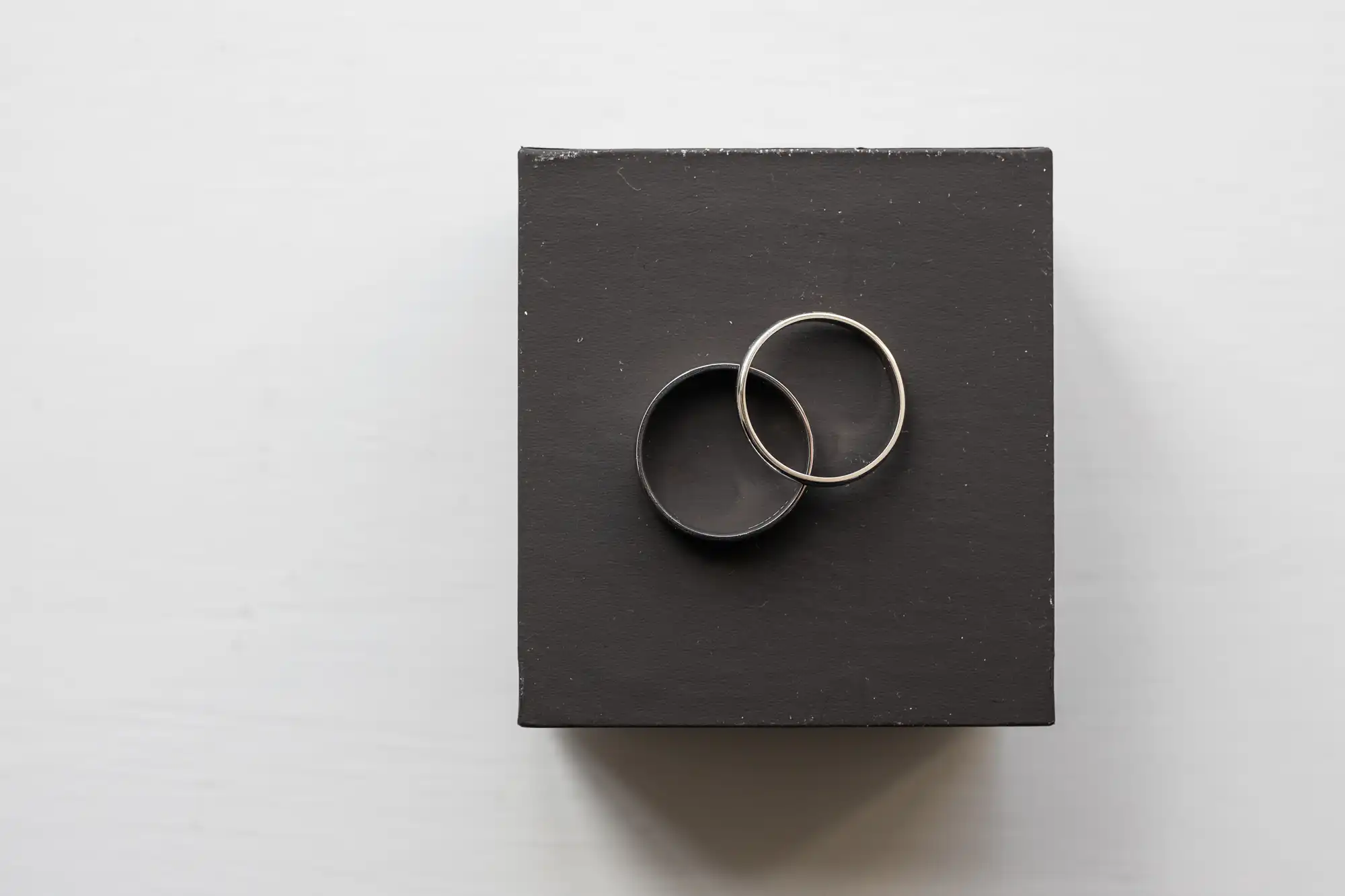 Two rings, one black and one silver, are placed on top of a black square box against a white background.