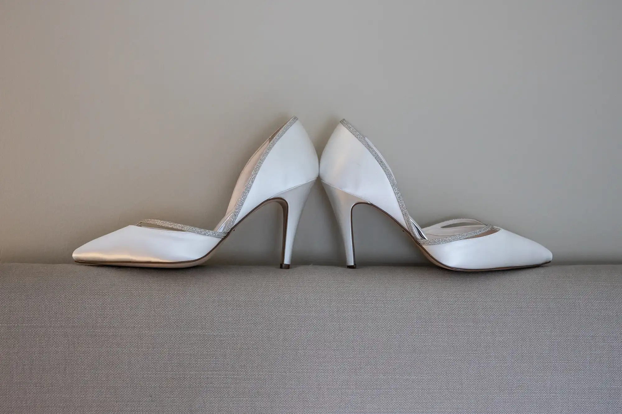 A pair of white high-heeled shoes placed back to back against a light gray background.