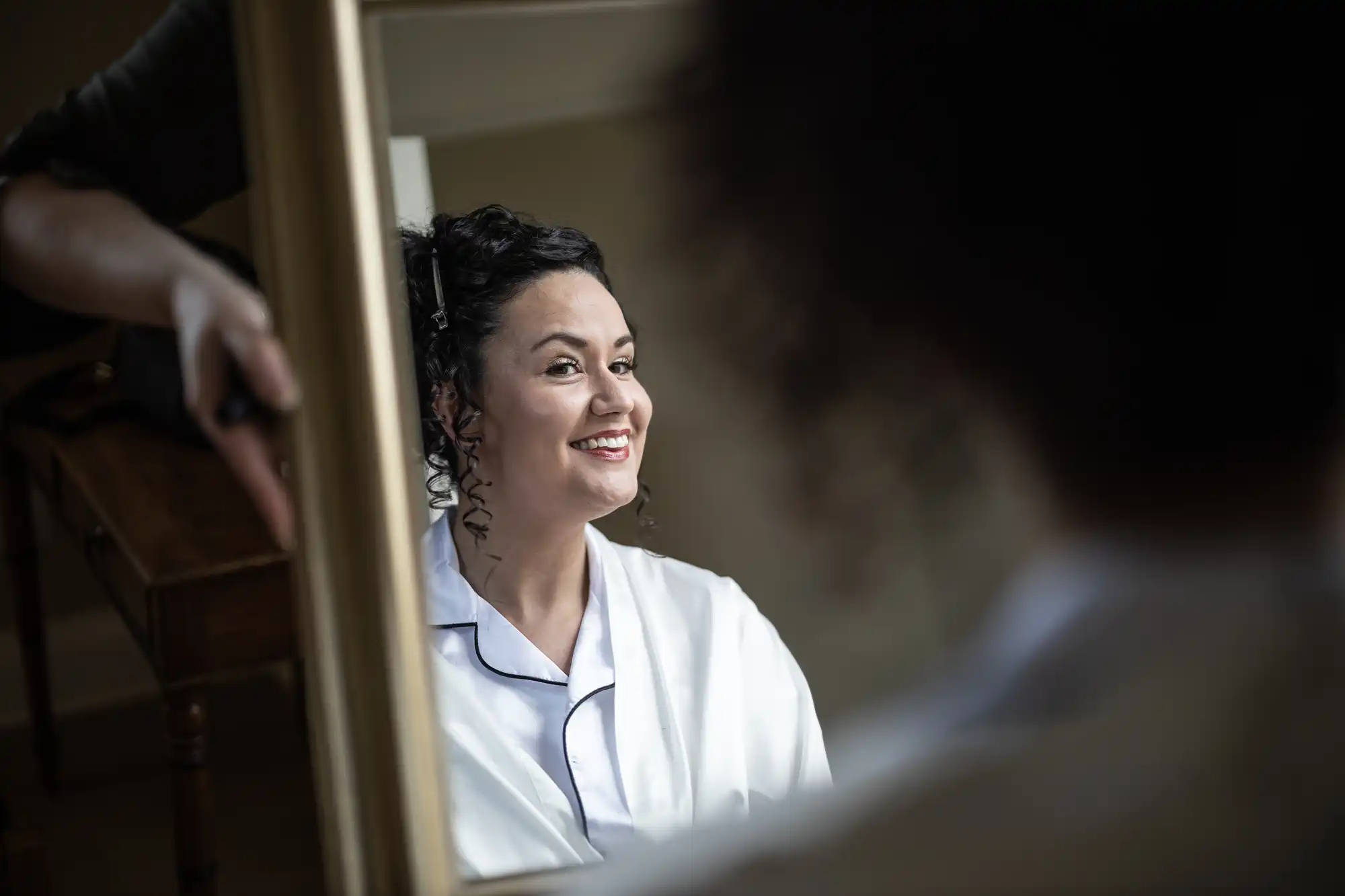 A woman wearing a white robe smiles while looking at herself in a mirror.