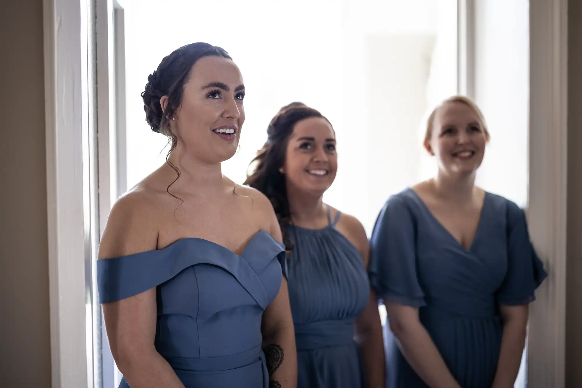 Three women in matching blue dresses stand and smile in a brightly lit room.