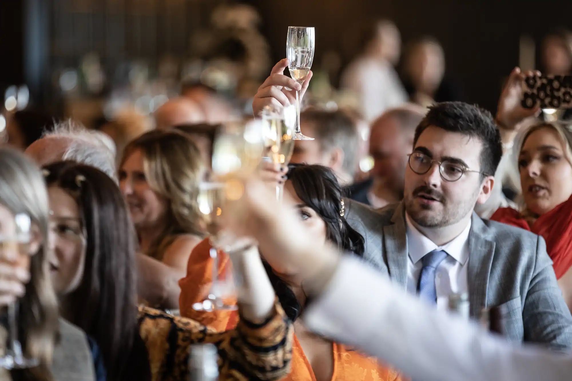 A group of people dressed in formal attire raise champagne glasses in a celebratory toast at an indoor gathering.