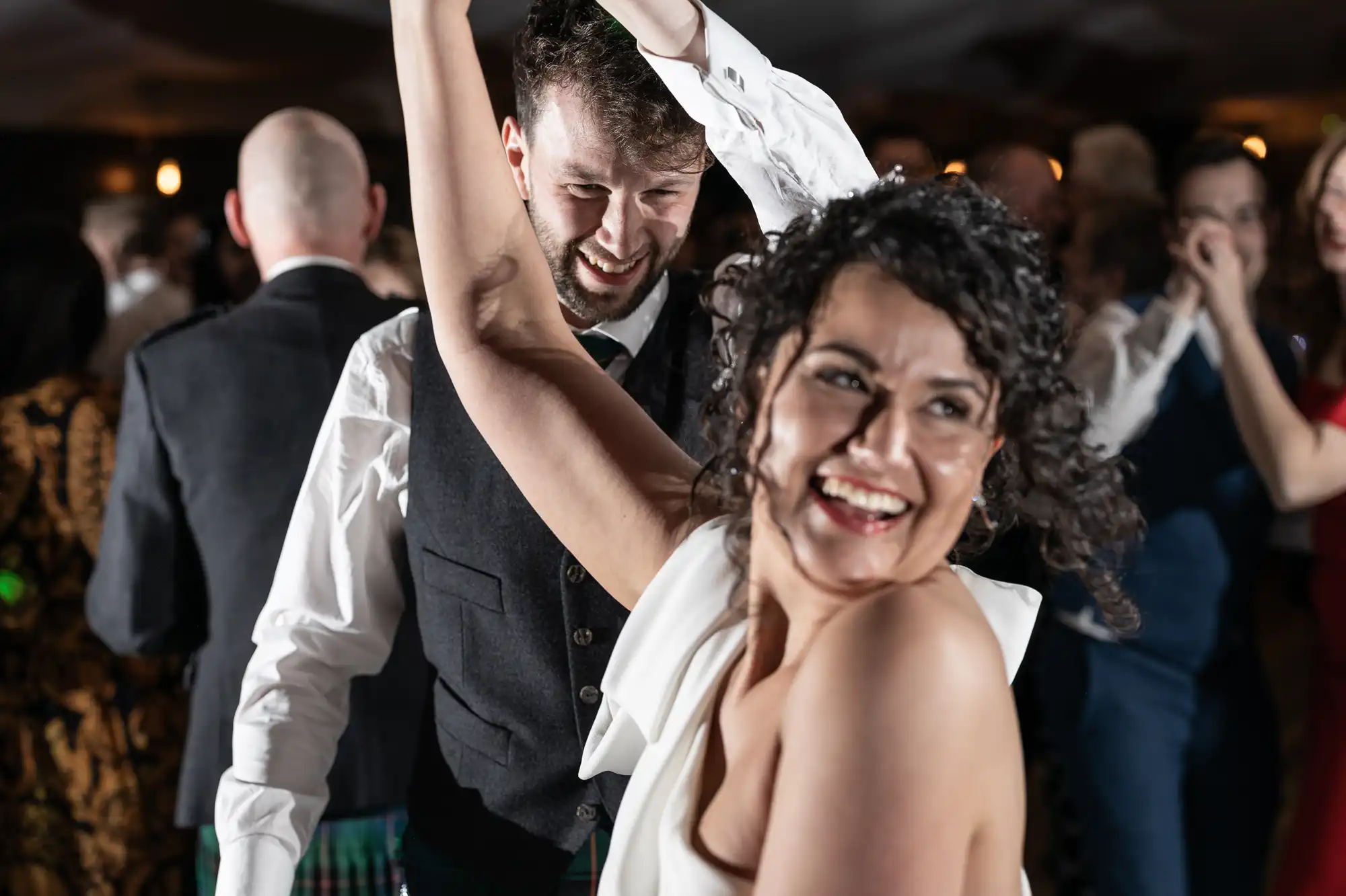 A joyful couple dances closely together at a lively indoor event, surrounded by other attendees.