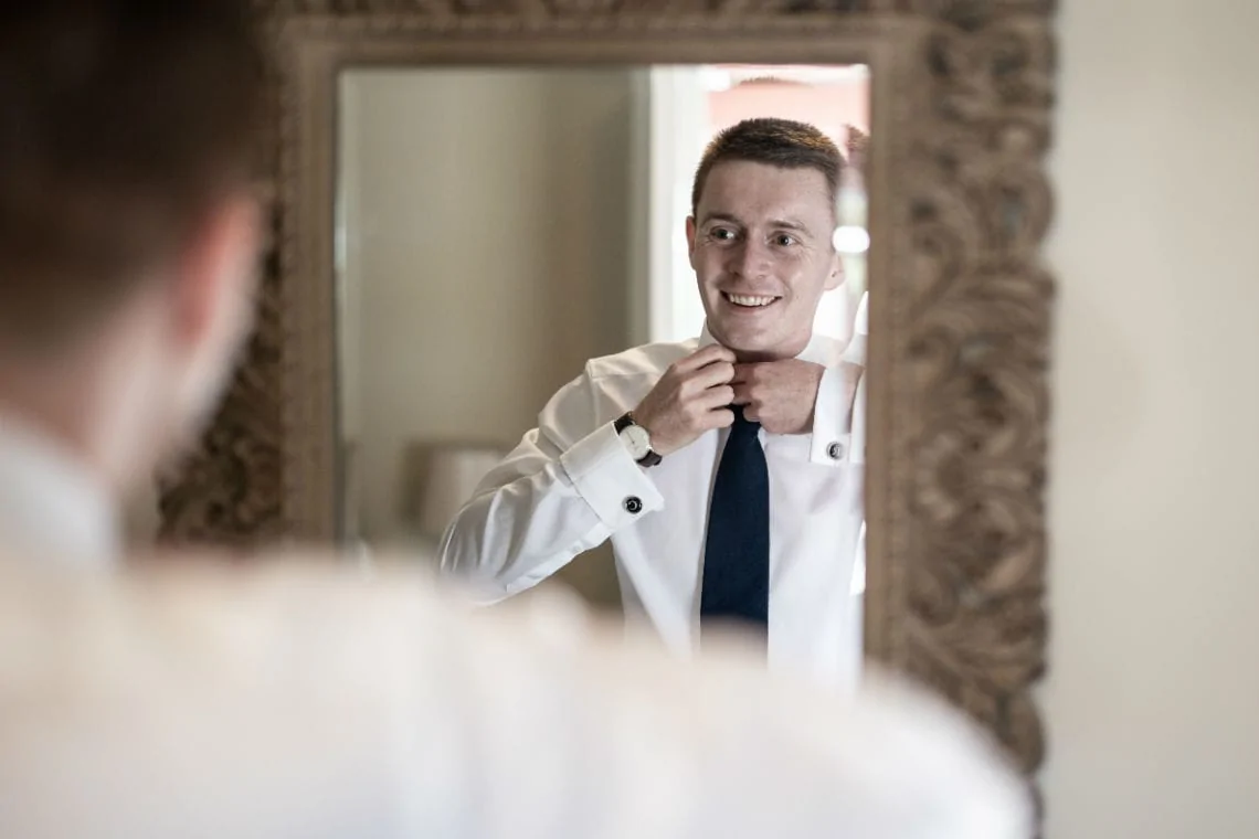 groom adjusting his tie looking in a mirror
