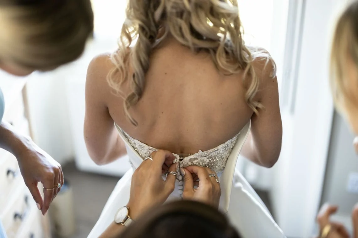 bride's dress being buttoned up by bridesmaid
