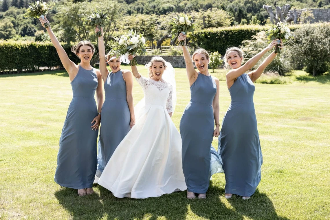 bride and bridesmaids cheer and hold their bouquets aloft outside Sea View House