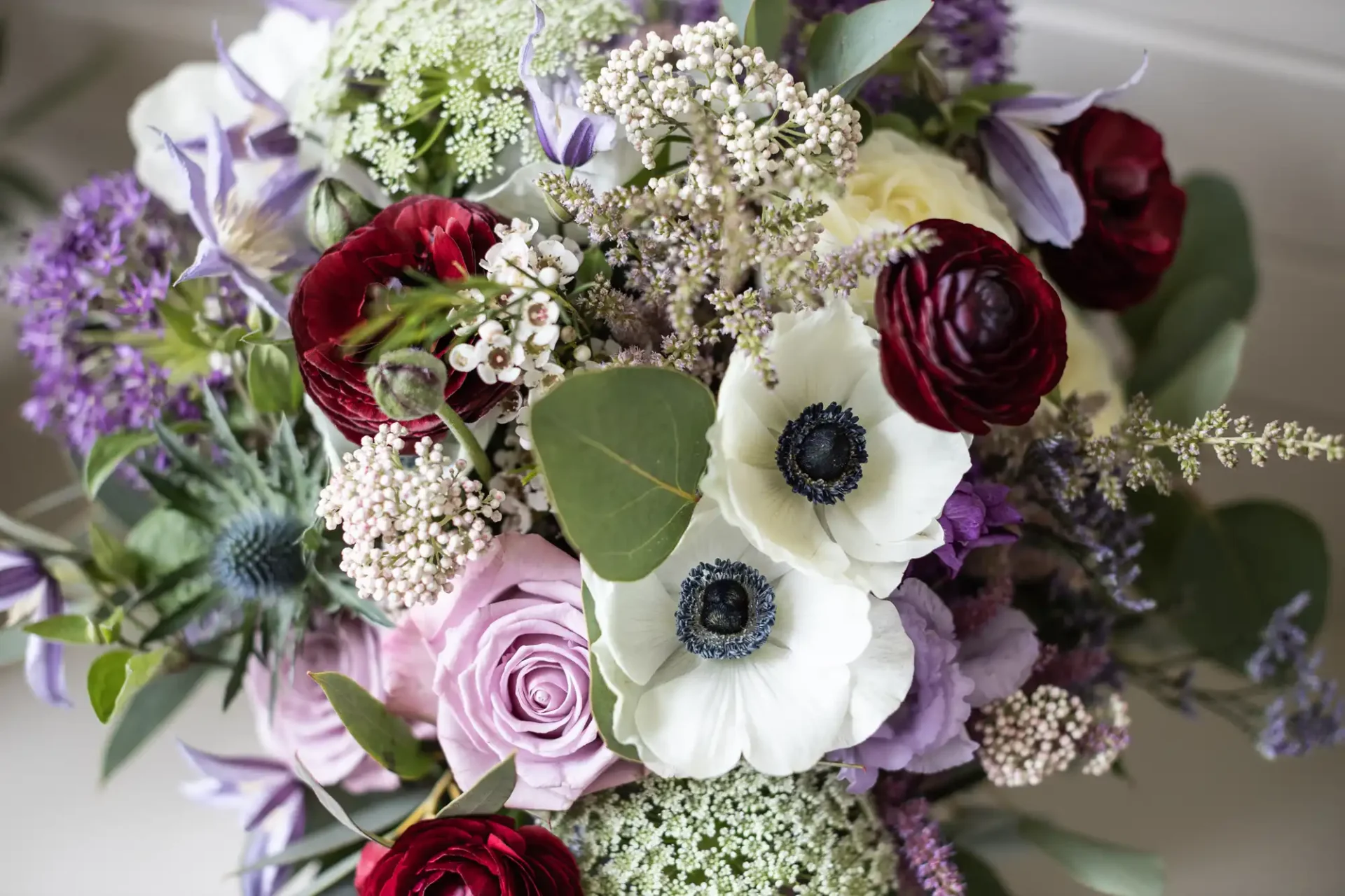 A floral arrangement featuring a mix of white, red, and purple flowers, including roses, anemones, and various greenery.