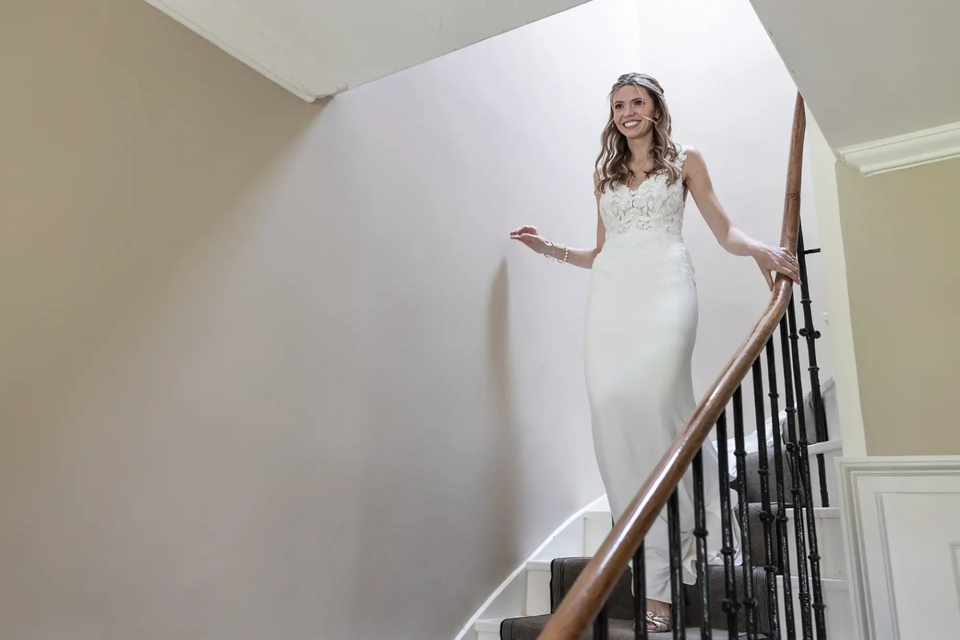 A woman in a white wedding dress smiles while walking down a staircase.