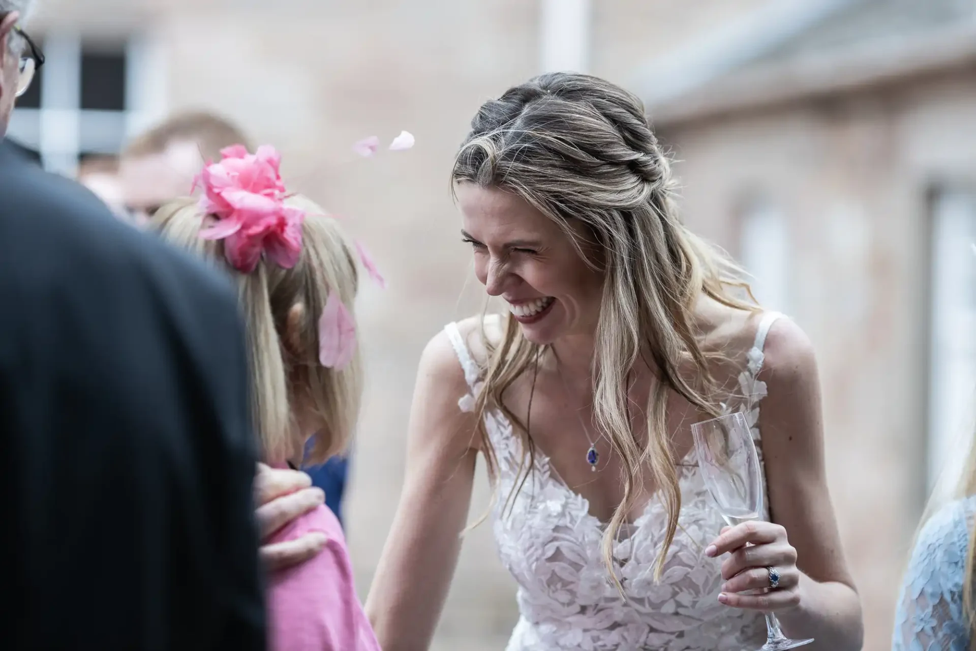 A smiling woman in a white dress interacts with another person wearing a pink outfit and headpiece at an outdoor event.