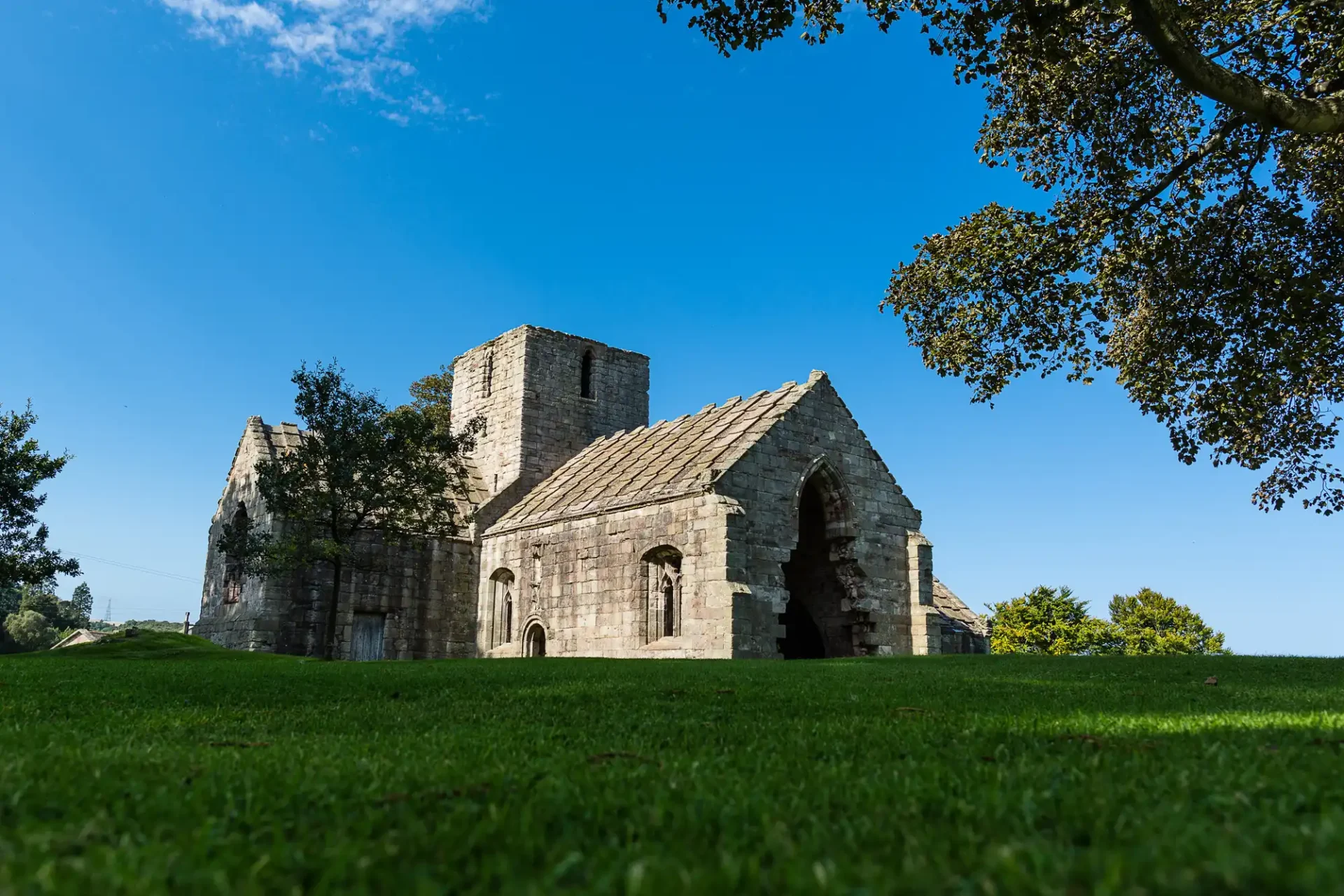 Dunglass Estate wedding photos ruins of an ancient stone building with a partial roof, surrounded by a grassy field and a large tree on the left under a clear blue sky.