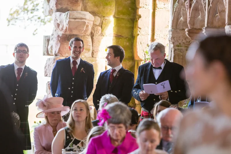 Guests smiling and glancing back during a wedding ceremony held in a historic stone building.