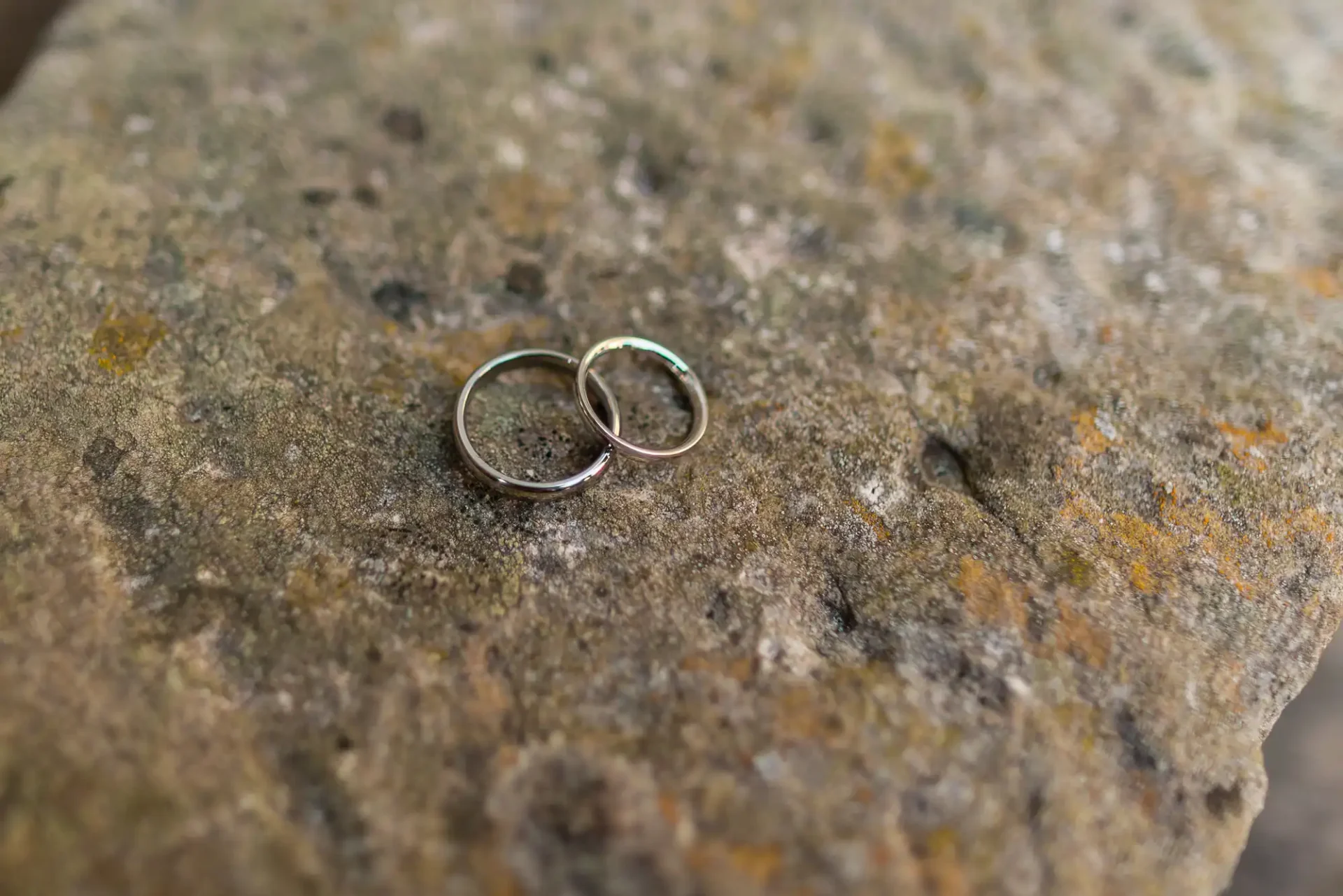 Two wedding rings placed on a weathered stone surface with patches of moss.