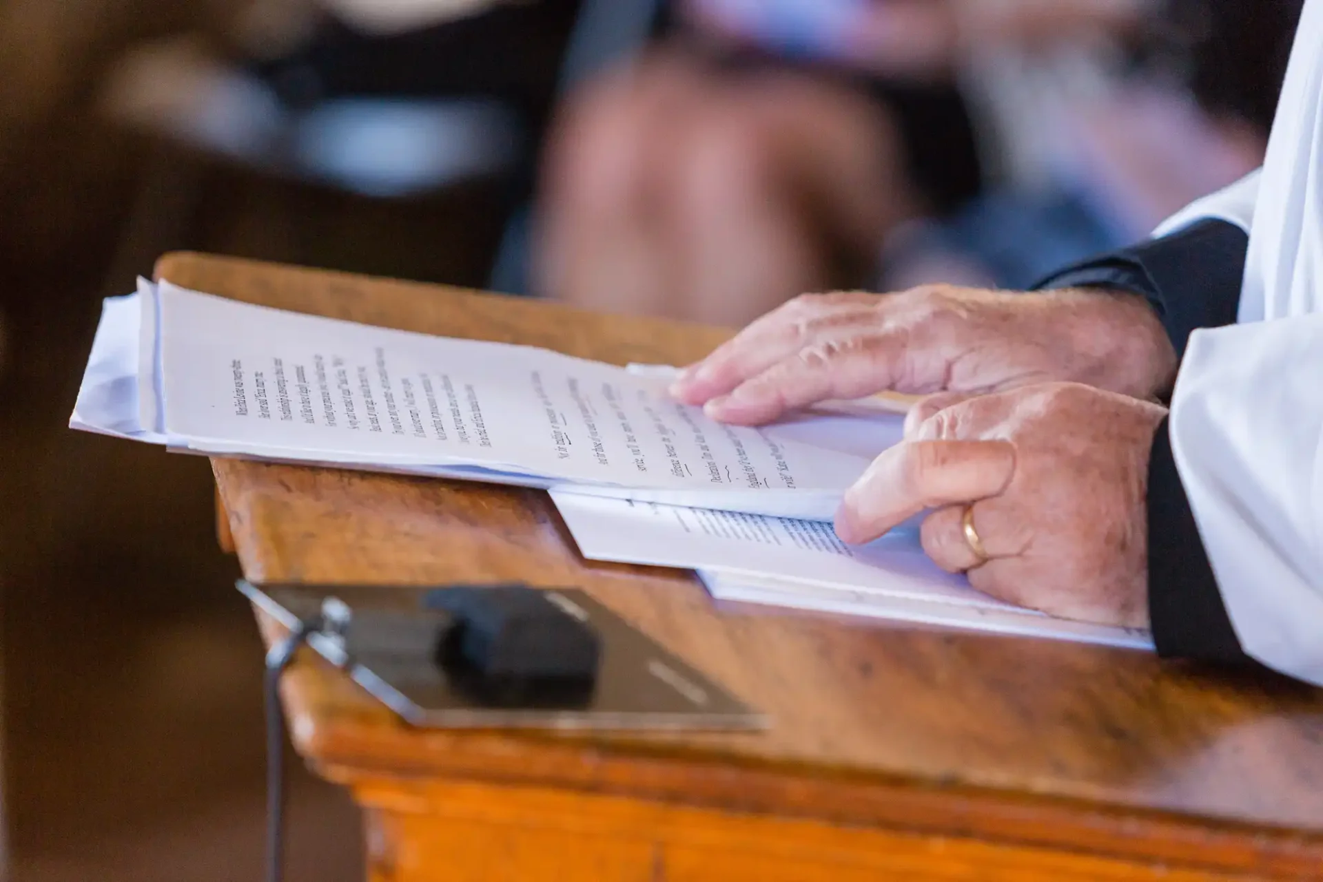 Close-up of a person's hands reading a document on a wooden lectern.