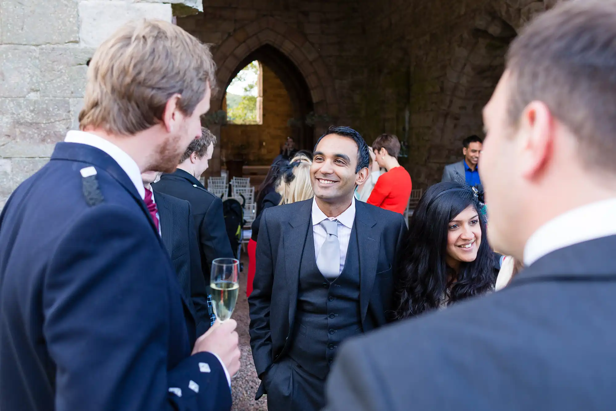 Group of people enjoying a conversation at an outdoor event, with one man smiling broadly, holding a glass of champagne.